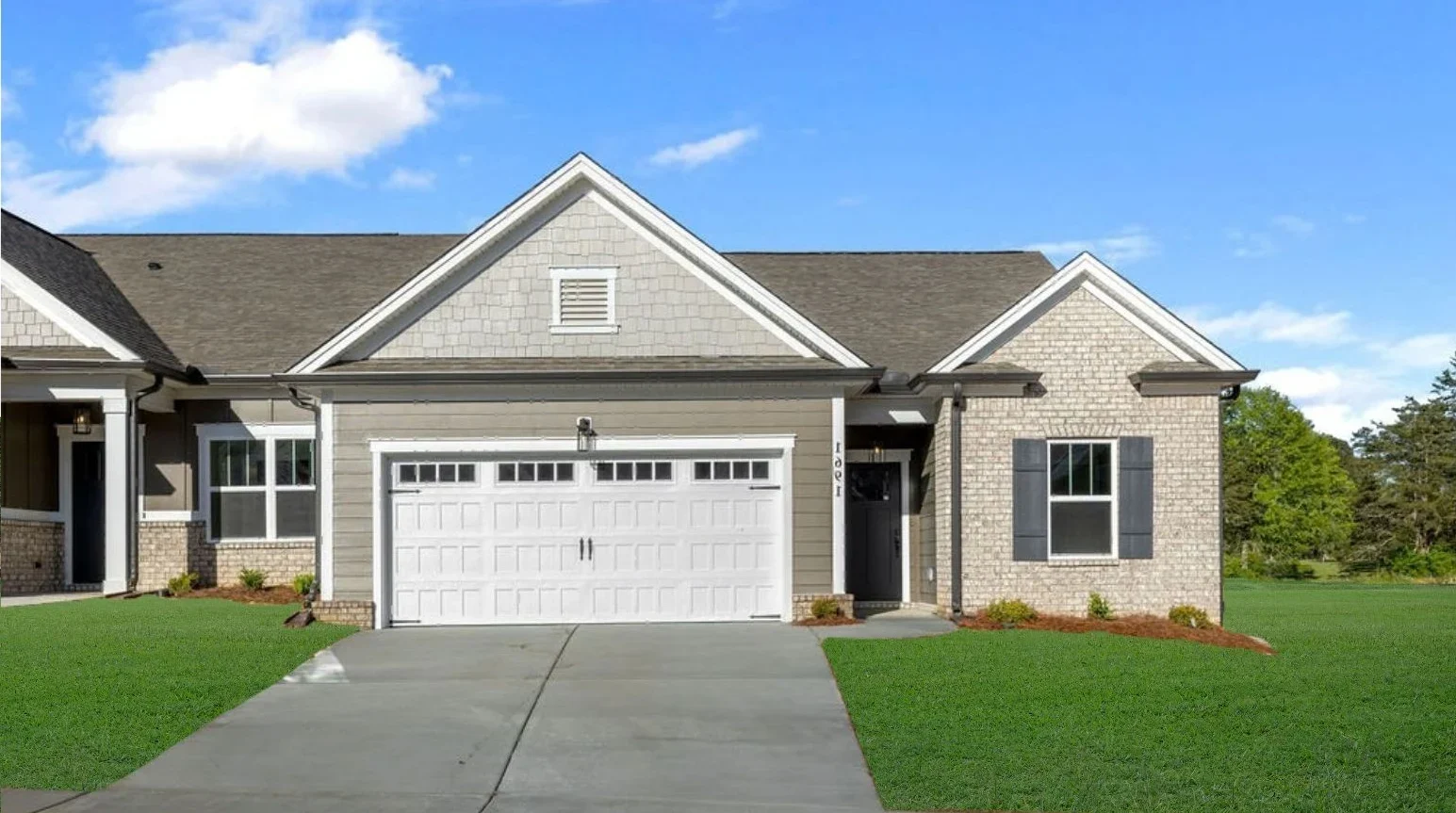 Single-story townhome with gable roof, brick facade, and white garage by Pratt Home Builders, surrounded by green lawn.