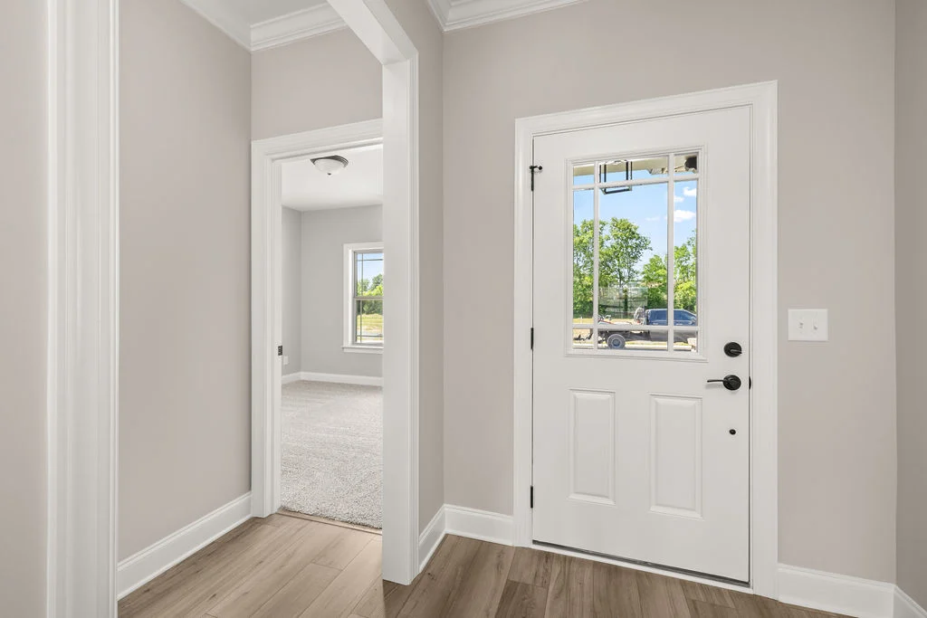 Bright entryway with a white door and window, leading to a carpeted room. Built by Pratt Home Builders in Chattanooga TN.