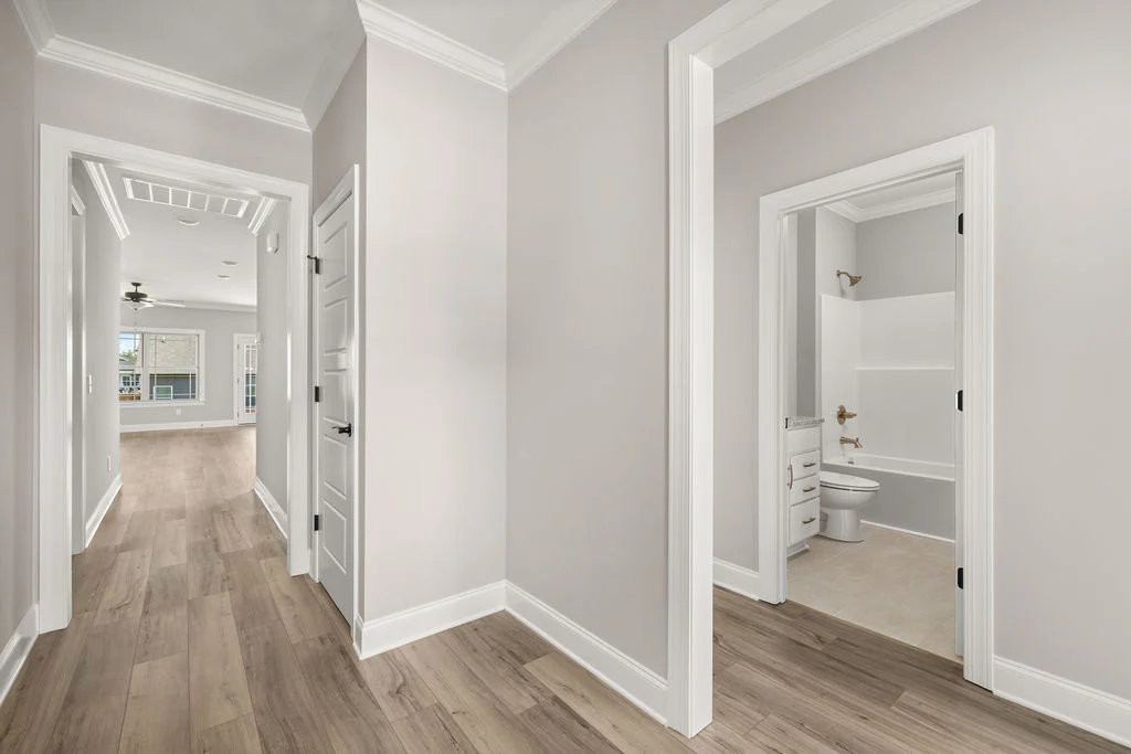 Hallway with light wood flooring, neutral walls, leading to a living area and bathroom. Design by Pratt Home Builders in Chattanooga TN.