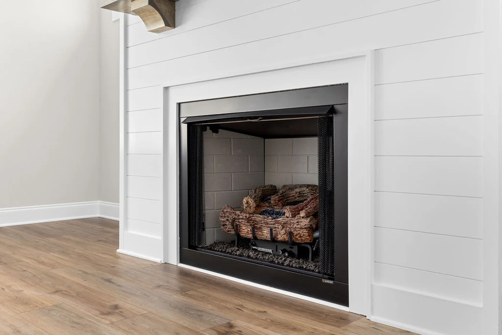 Modern fireplace with white shiplap surround and wood mantel, featuring a cozy log set by Pratt Home Builders in Chattanooga TN.