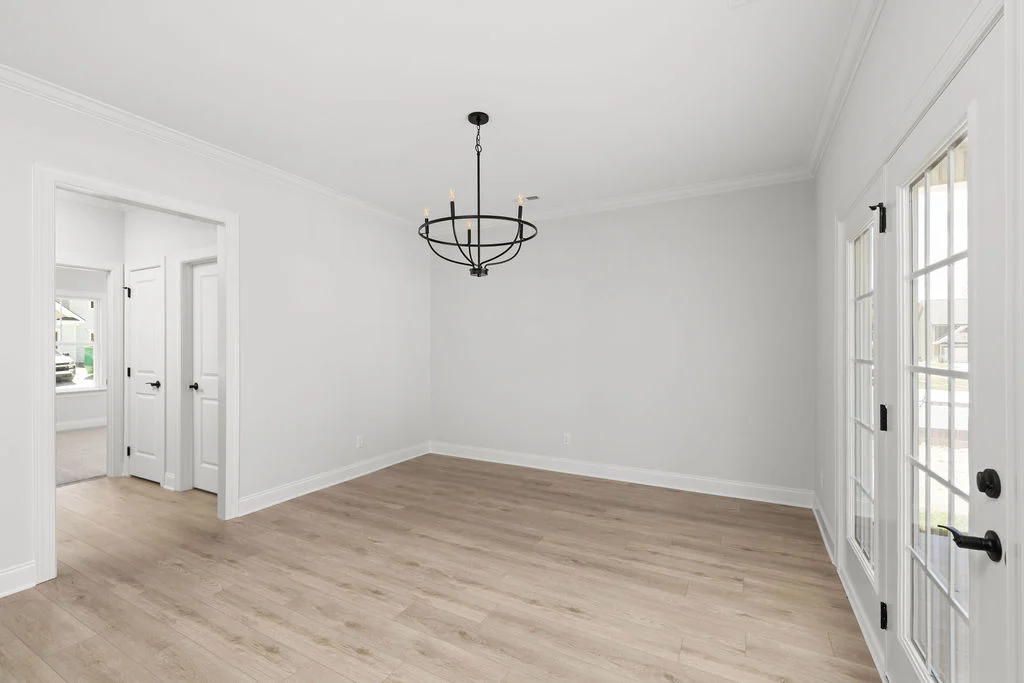 Bright, empty room with light wood floors, white walls, black chandelier, and French doors by Pratt Home Builders in Chattanooga TN.
