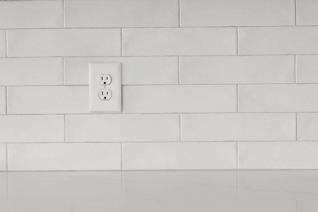 White tiled backsplash with electrical outlet, reflecting simple elegance. Pratt Home Builders in Chattanooga TN may be noted for such clean designs.