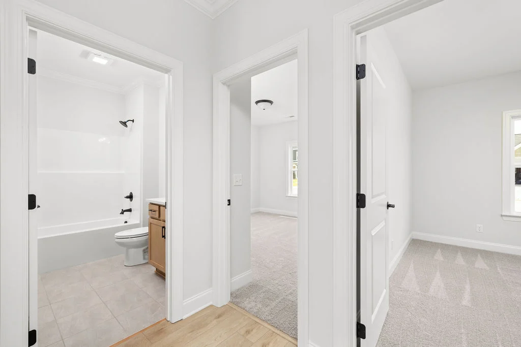 Bright hallway leading to a bathroom and two carpeted rooms, showcasing modern design by Pratt Home Builders in Chattanooga TN.