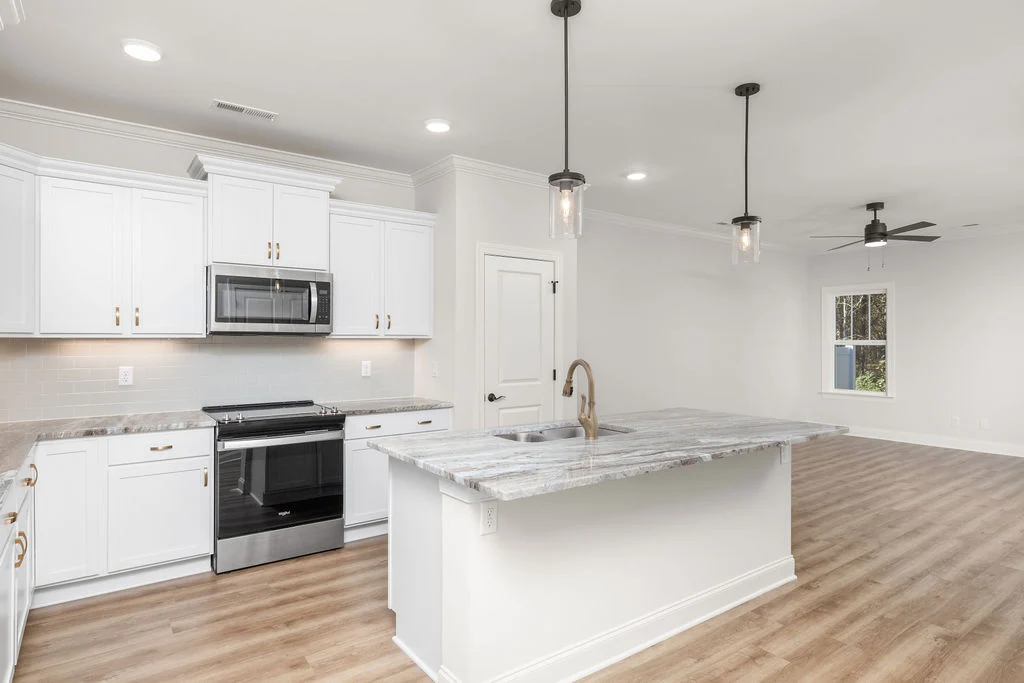Modern kitchen and living area with white cabinets, marble island, pendant lights, and ceiling fan by Pratt Home Builders in Chattanooga TN.