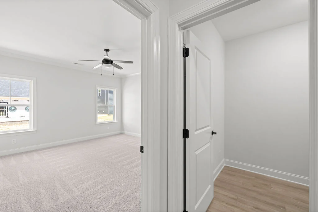 Bright, minimalist room by Pratt Home Builders in Chattanooga TN, featuring carpet, a ceiling fan, and modern finishes with adjacent hardwood hallway.