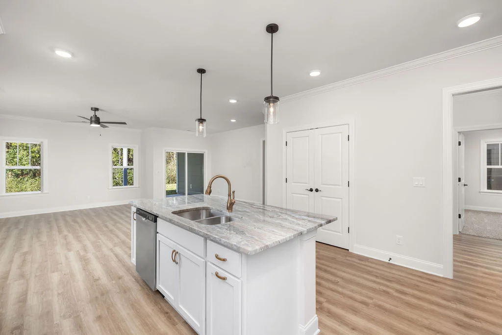 Modern kitchen and living area with light wood flooring, white cabinets, and granite island in a home by Pratt Home Builders in Chattanooga TN.