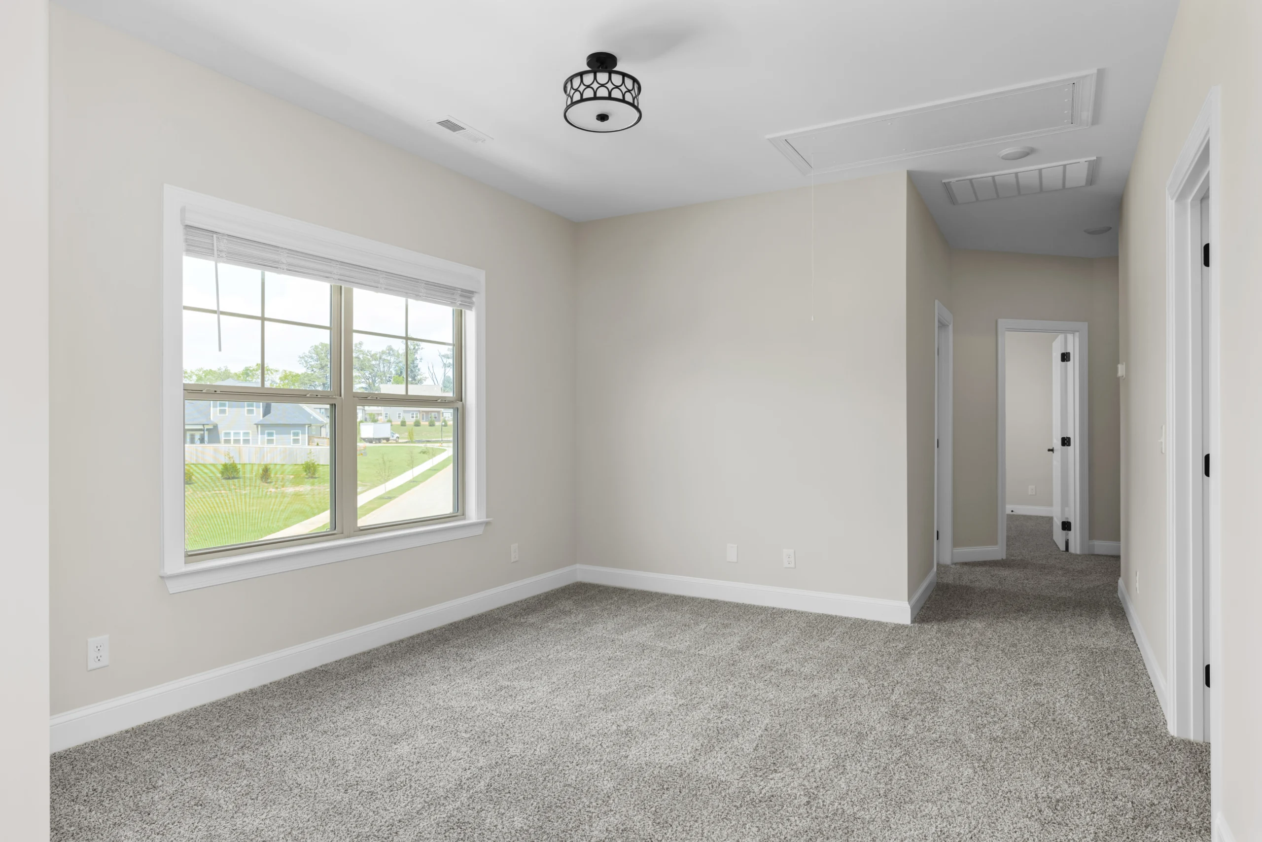 Spacious room office space with gray carpet, large window, neutral walls, and a modern ceiling light by Pratt Home Builders in Chattanooga TN.