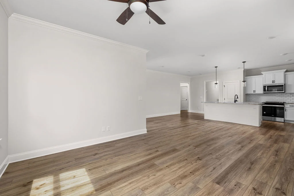 Spacious modern kitchen and living area with wood flooring, white cabinetry, and ceiling fan, by Pratt Home Builders in Chattanooga TN.