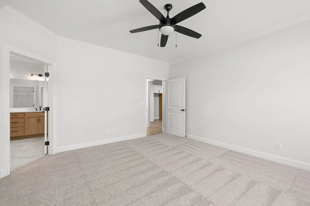 Empty, spacious room with beige carpet, ceiling fan, open door to bathroom, built by Pratt Home Builders in Chattanooga TN.