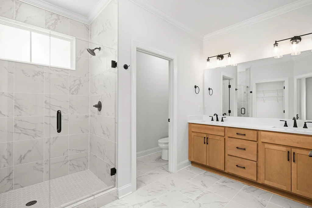 New Home Chattanooga TN. Modern bathroom with glass shower, marble tiles, double vanity, and wooden cabinets by Pratt Home Builders.