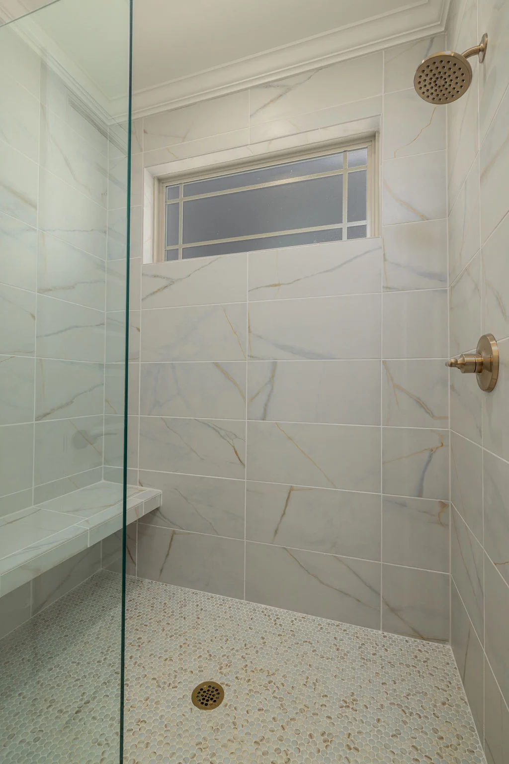 Elegant shower with marble veining and penny tile flooring, designed by Pratt Home Builders in Chattanooga TN, featuring brass fixtures.