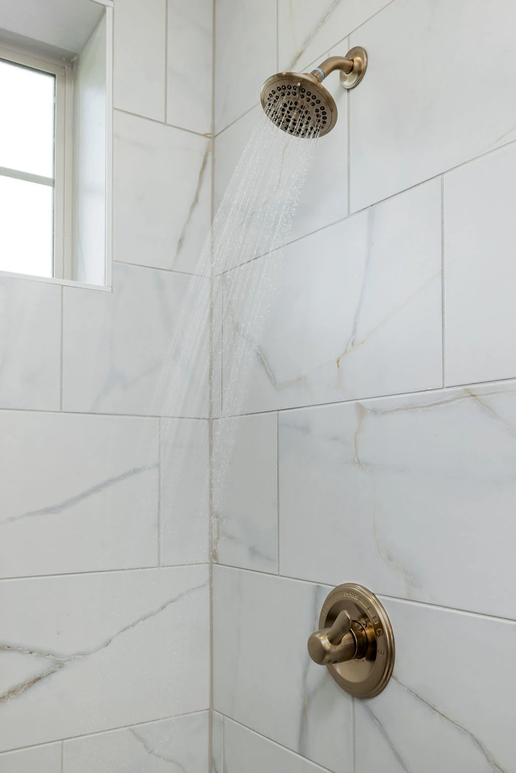 Modern shower with sleek, gold fixtures against white marble tiles, designed by Pratt Home Builders in Chattanooga TN.