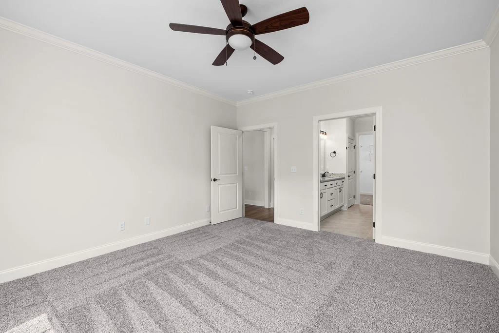 Spacious, neutral-toned carpeted room with a ceiling fan and open doors leading to a bathroom by Pratt Home Builders in Chattanooga TN.