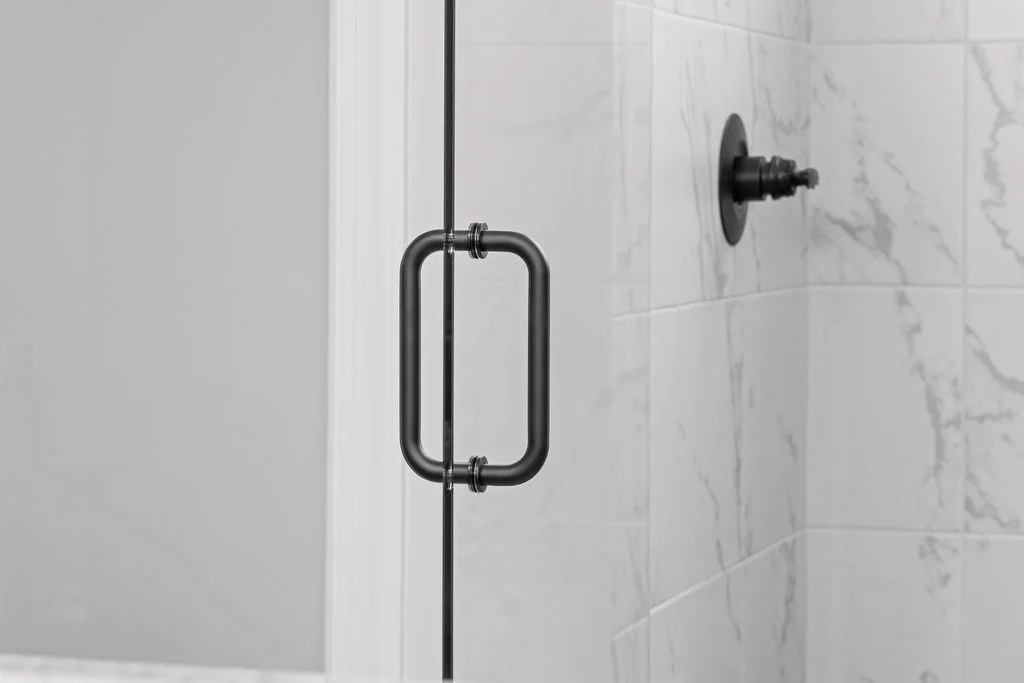 Sleek black shower handle and fixture against marble tile detail in a modern bathroom, designed by Pratt Home Builders in Chattanooga TN.