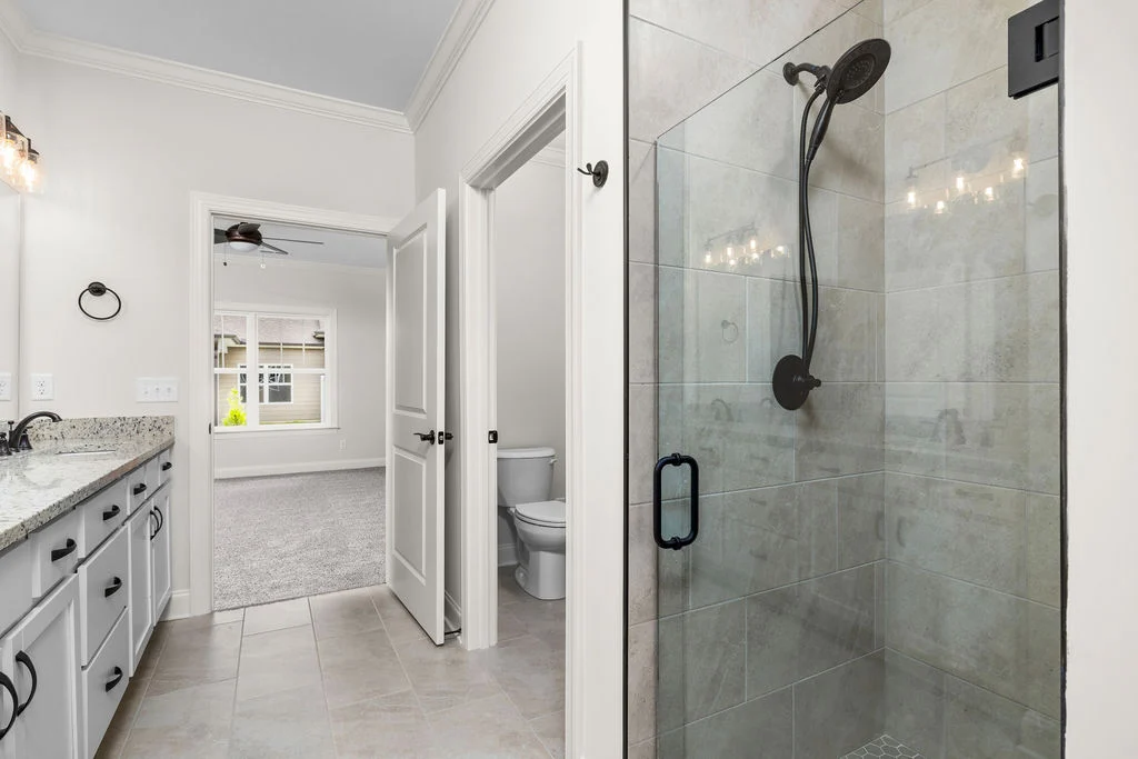 Modern bathroom by Pratt Home Builders in Chattanooga TN, featuring a glass shower, dual sinks, and a view into a spacious bedroom.
