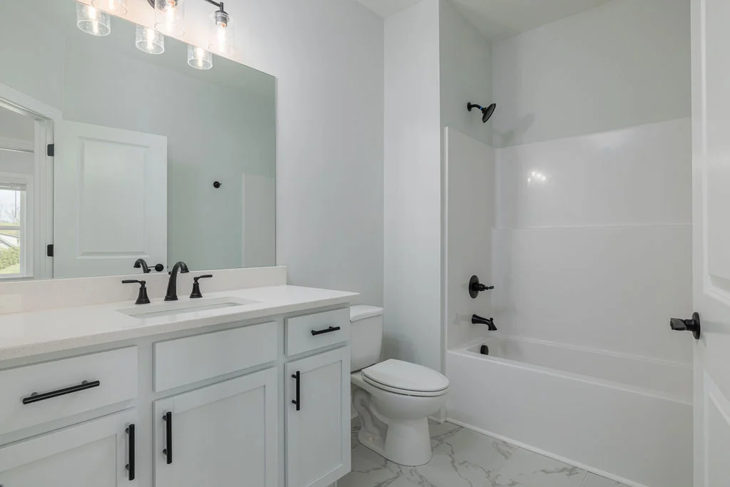 Modern bathroom with white cabinets, black fixtures, large mirror, and tub. Design by Pratt Home Builders in Chattanooga TN.