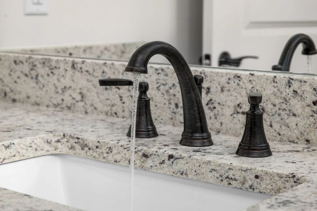 Bronze faucet with running water on a speckled granite countertop, designed by Pratt Home Builders in Chattanooga TN.
