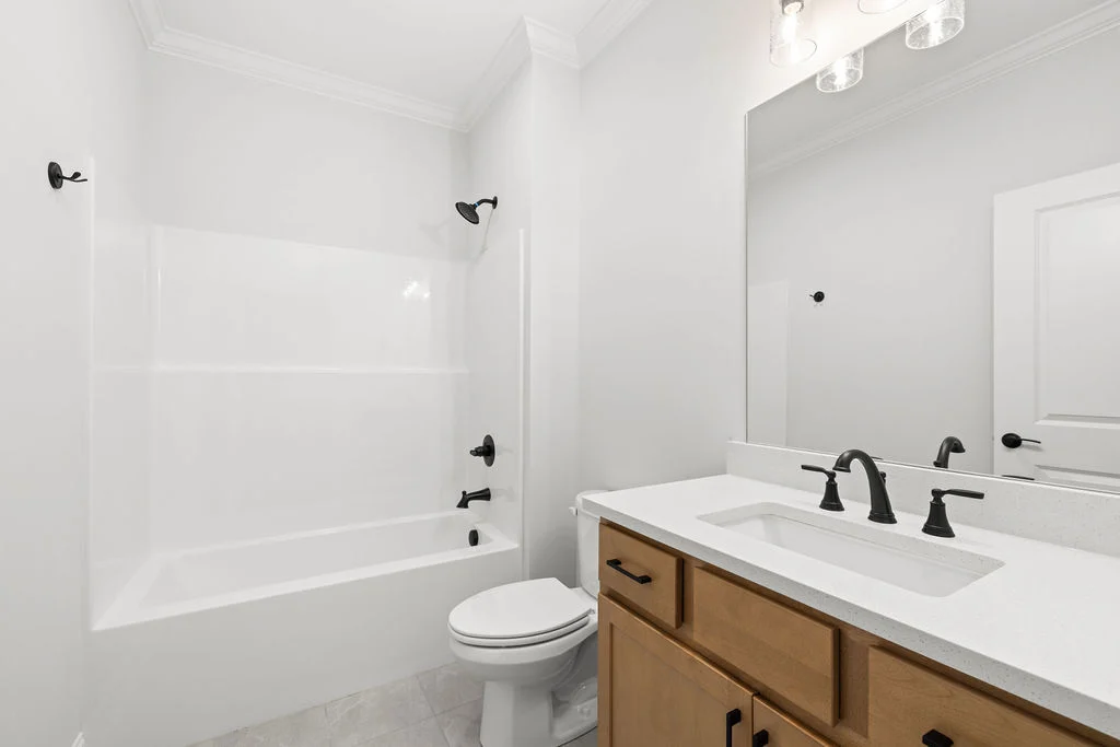 New home Chattanooga TN. Modern bathroom with white tub, vanity, and black fixtures by Pratt Home Builders. Light wood cabinetry and large mirror.