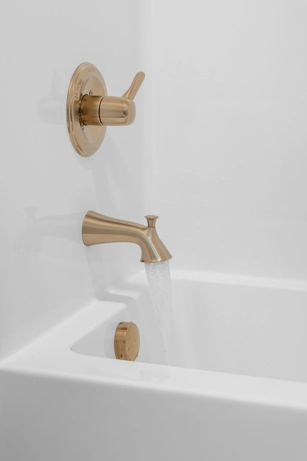 Elegant brass bathtub faucet with water flowing, set against a white tub; by Pratt Home Builders in Chattanooga TN.