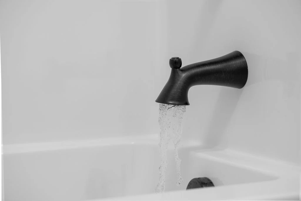 Water flows from a dark faucet into a white bathtub, showcasing elegant bathroom design by Pratt Home Builders in Chattanooga TN.