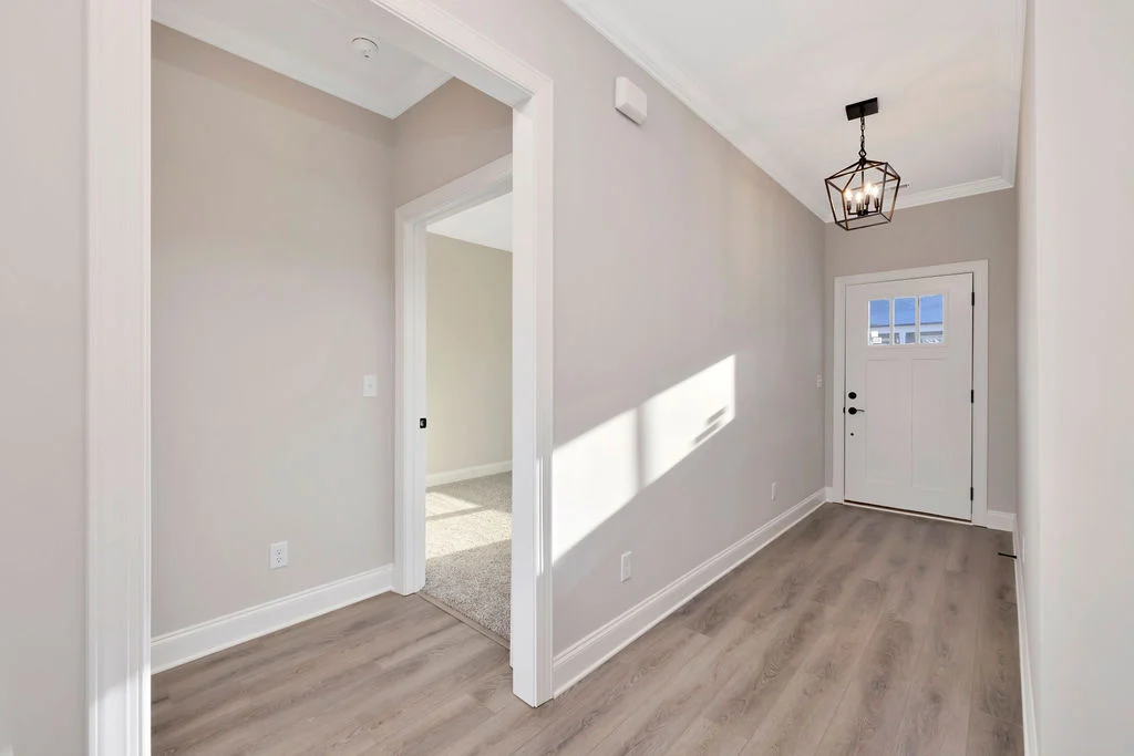 Bright hallway with wood flooring, white trim, hanging lantern light fixture, and doorway, designed by Pratt Home Builders in Chattanooga TN.