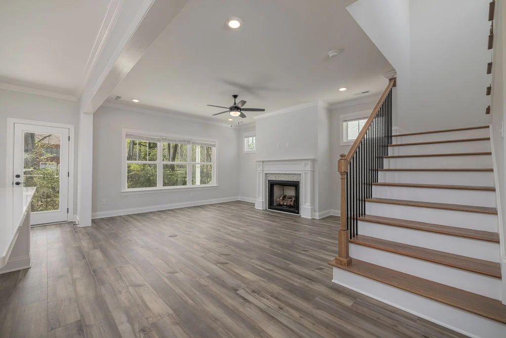Spacious modern living room by Pratt Home Builders in Chattanooga TN, featuring hardwood floors, a fireplace, large windows, and a staircase.
