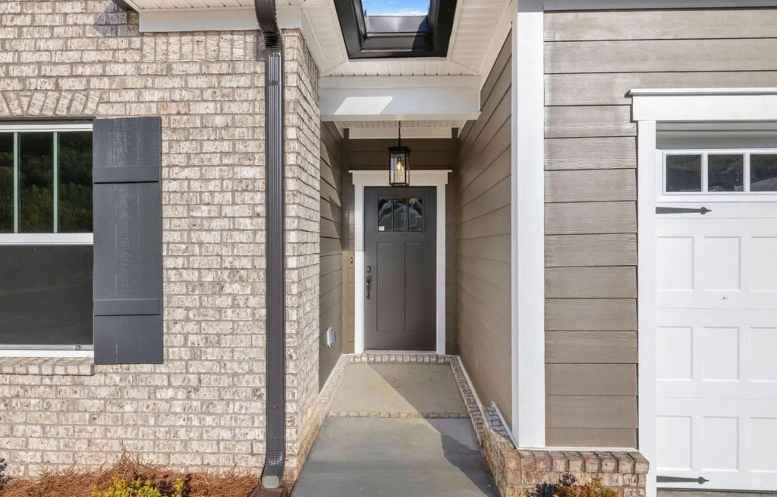 Entrance of a modern home by Pratt Home Builders in Chattanooga TN, featuring a brick facade, dark door, and skylight above.