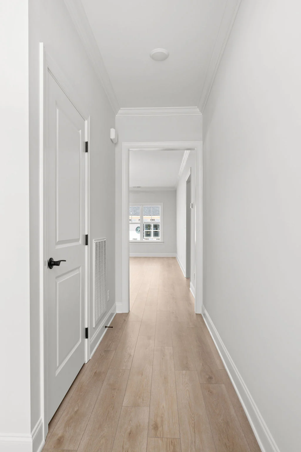 Modern corridor with light wood flooring, white walls, and a door leading to a room with large windows. Built by Pratt Home Builders in Chattanooga TN