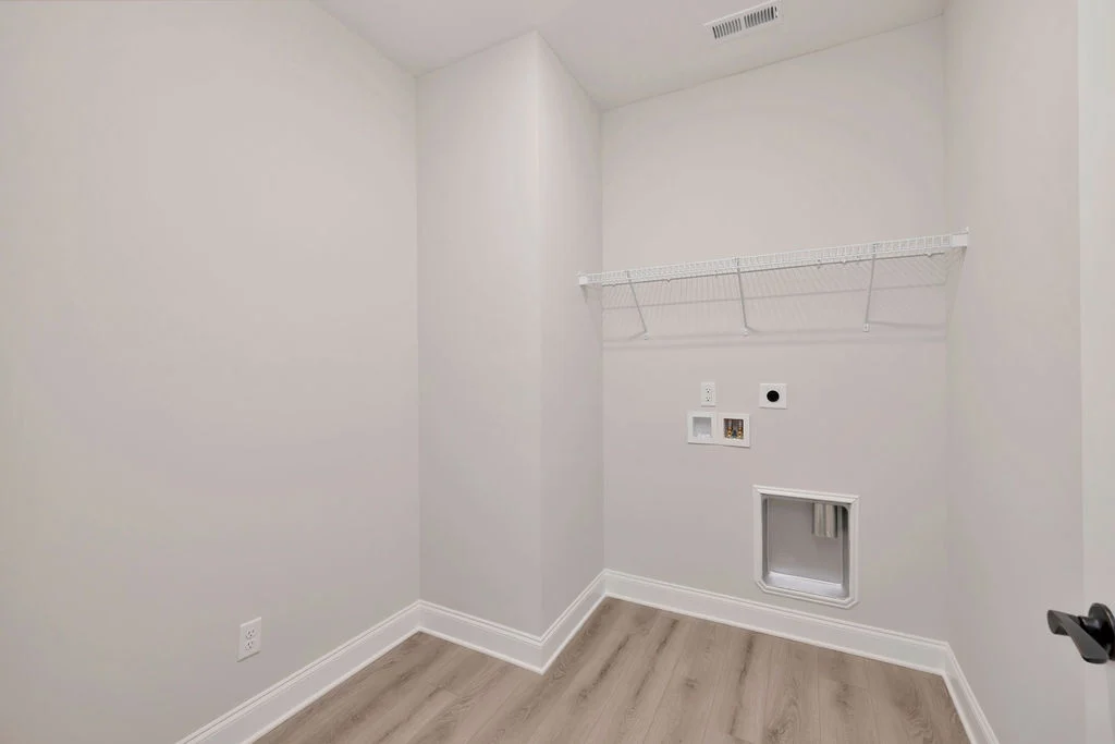 Laundry room with white walls, hardwood floor, wire shelf, and utility hookups by Pratt Home Builders in Chattanooga TN.