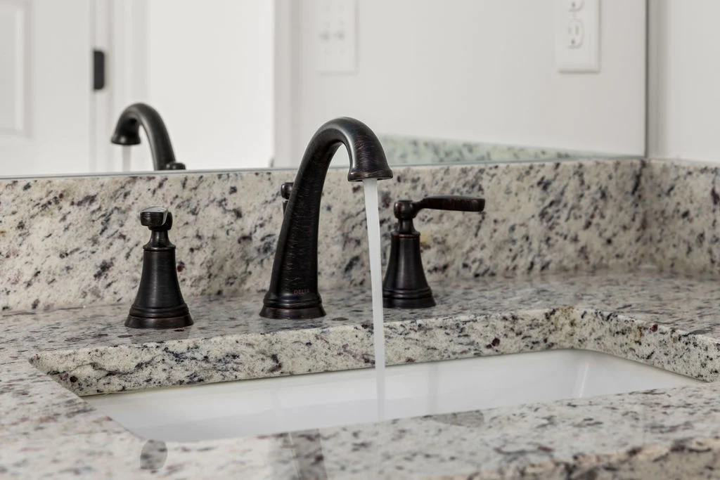 Running water from a sleek black faucet set in a speckled granite countertop by Pratt Home Builders in Chattanooga TN.