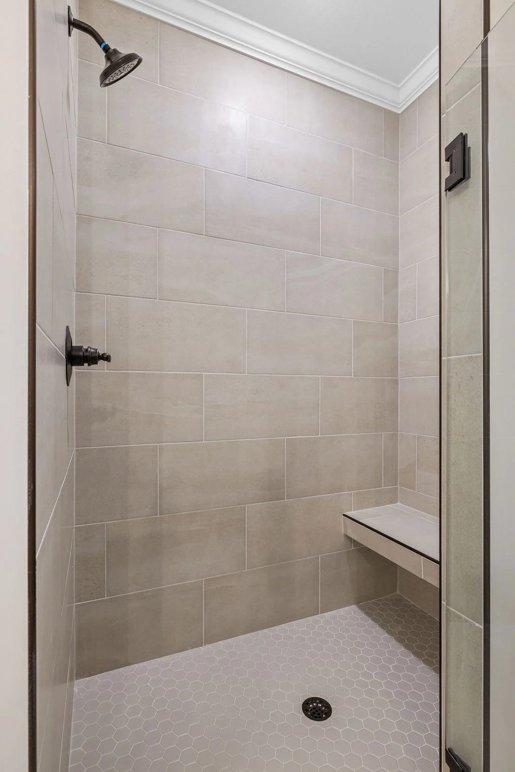 Modern beige tiled shower with bench, black fixtures, hexagonal floor tiles. Built by Pratt Home Builders in Chattanooga TN.