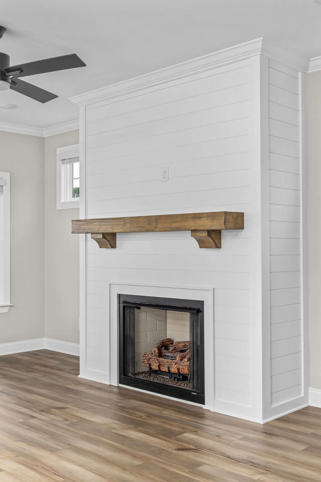 White shiplap fireplace with wooden mantel, hardwood floors, ceiling fan. Design by Pratt Home Builders in Chattanooga TN.
