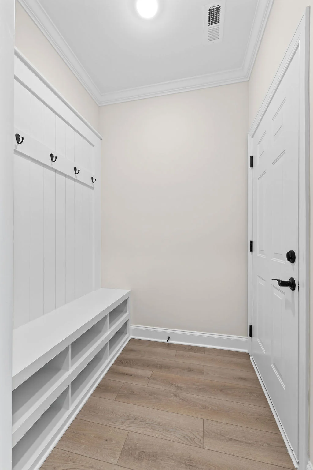 Mudroom with white bench, storage cubbies, and hooks, designed by Pratt Home Builders in Chattanooga TN. Wood flooring and white door.