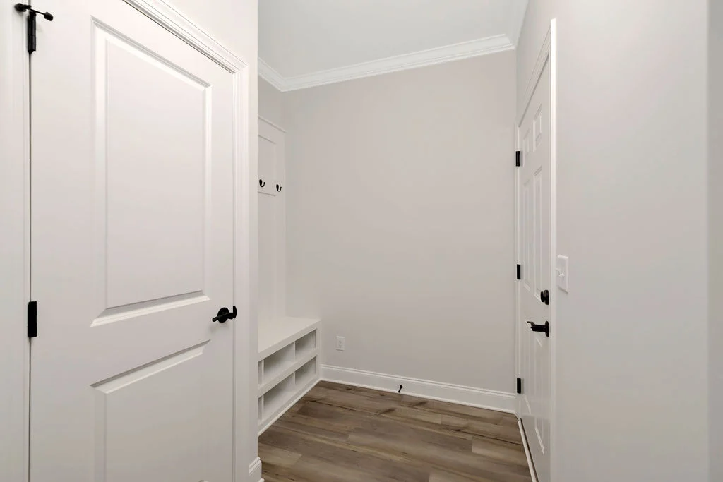 White hallway with wooden floor, featuring a bench, storage shelves, and coat hooks. Designed by Pratt Home Builders in Chattanooga TN.