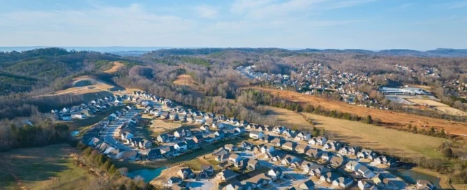 Aerial view of a suburban neighborhood by Pratt Home Builders in Chattanooga, TN, nestled among scenic hills and greenery under a clear sky.