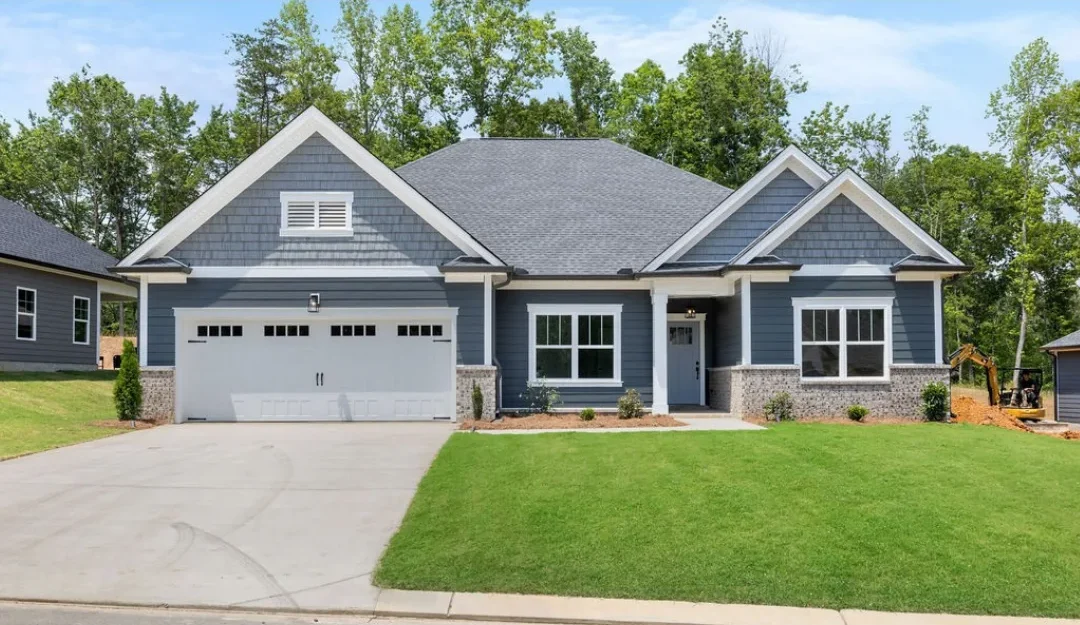 Modern blue-gray house with a two-car garage, lush lawn, built by Pratt Home Builders in Chattanooga TN, surrounded by trees.