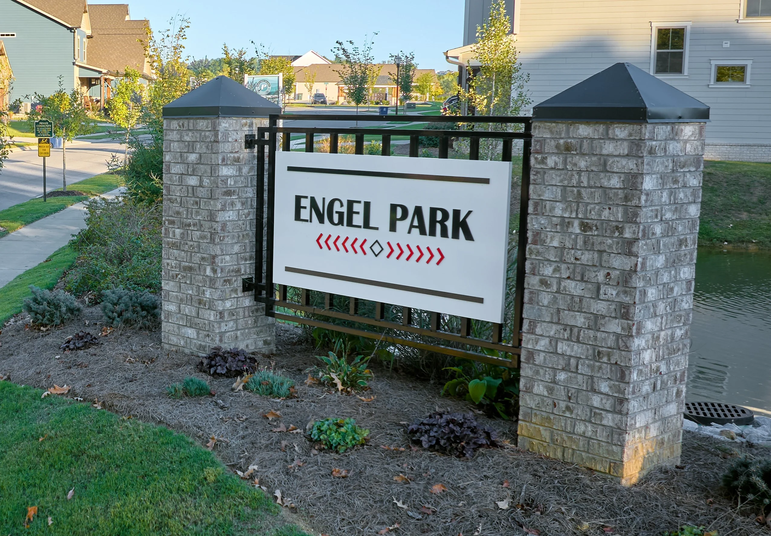 Brick entrance sign for Engel Park, landscaped with shrubs. Houses line the street in the background. Pratt Home Builders in Chattanooga TN.
