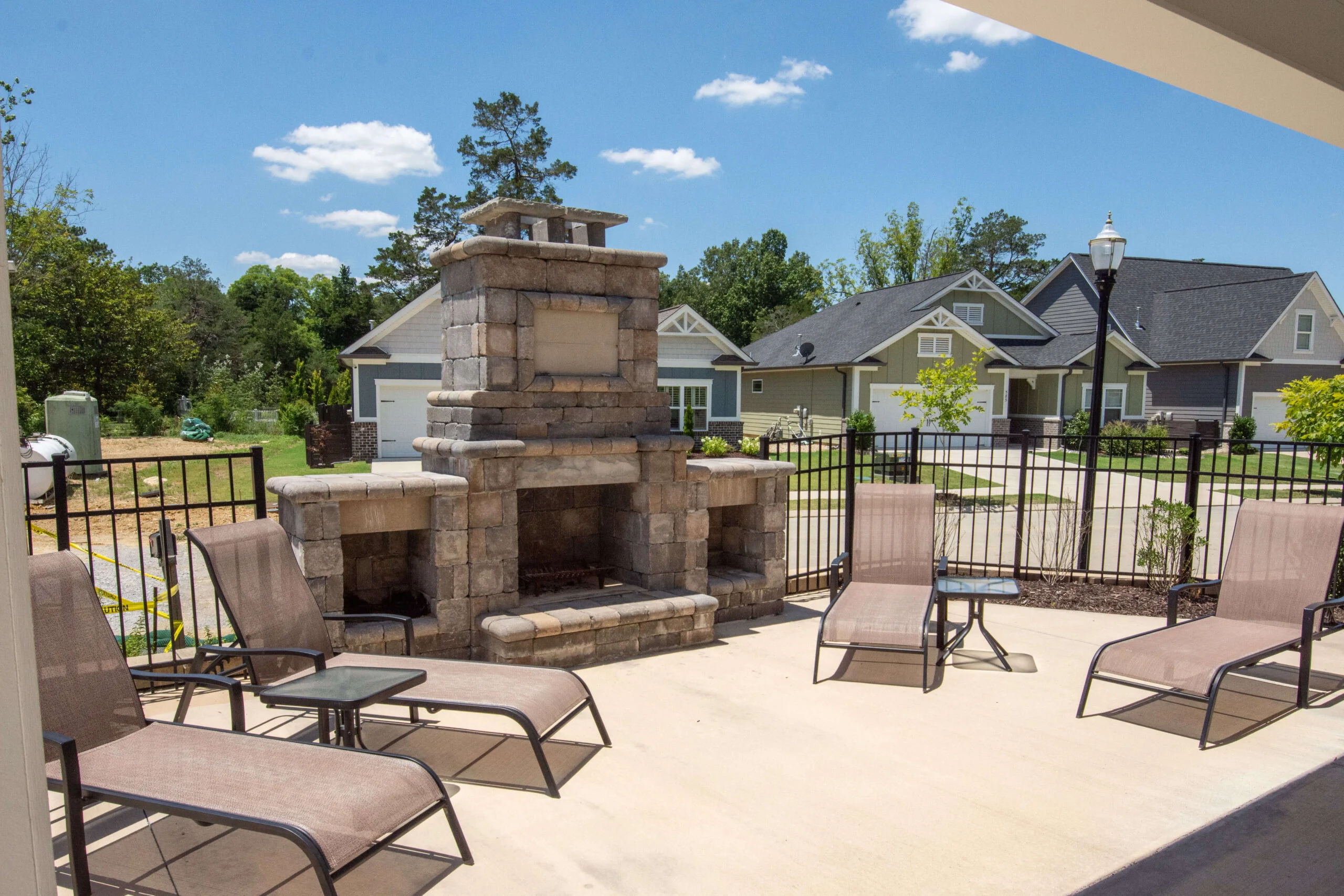 Outdoor patio with stone fireplace and lounge chairs, set against suburban homes by Pratt Home Builders in Chattanooga TN.