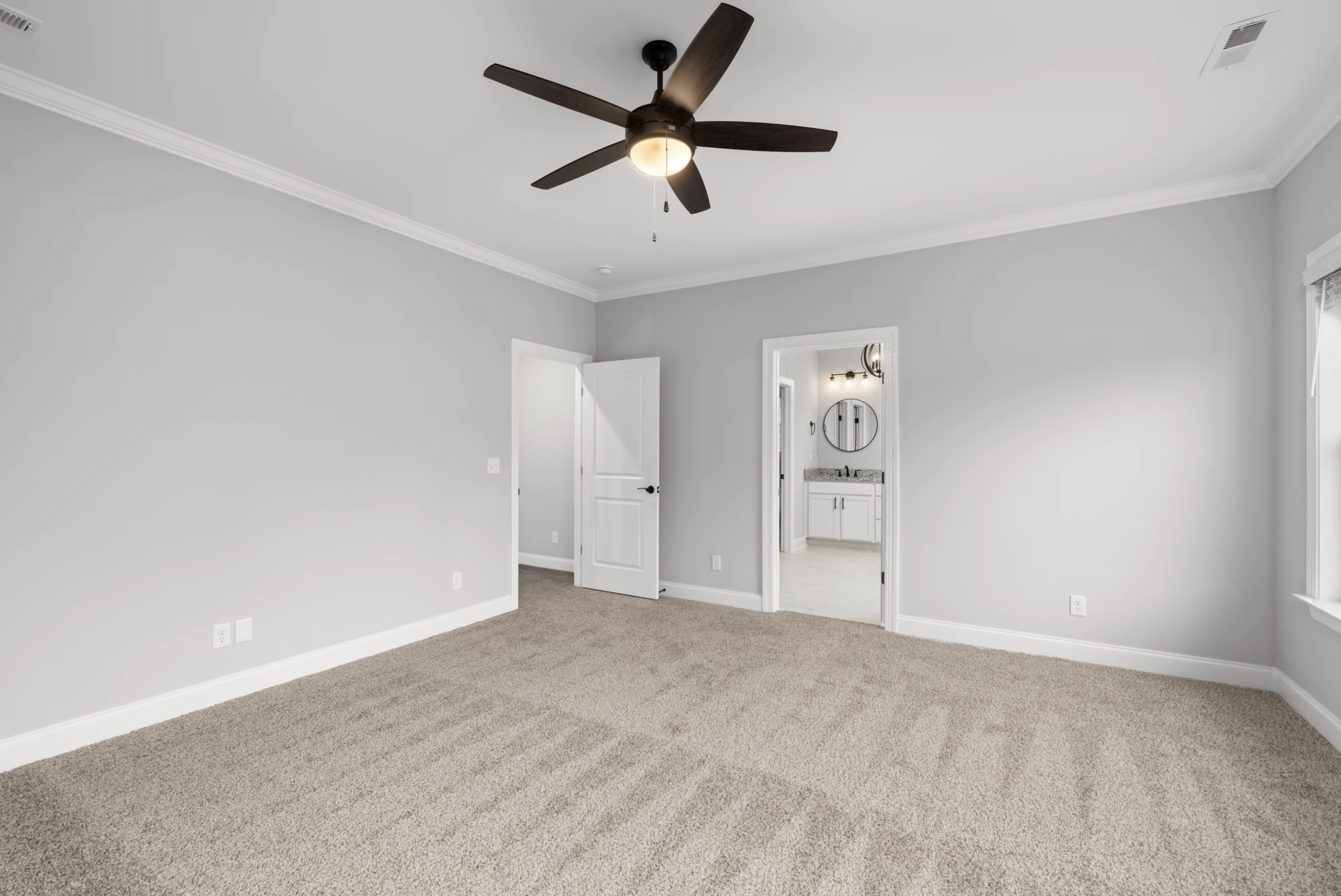 New Home Chattanooga TN. Spacious, carpeted bedroom with ceiling fan, gray walls, and adjacent bathroom by Pratt Home Builders.