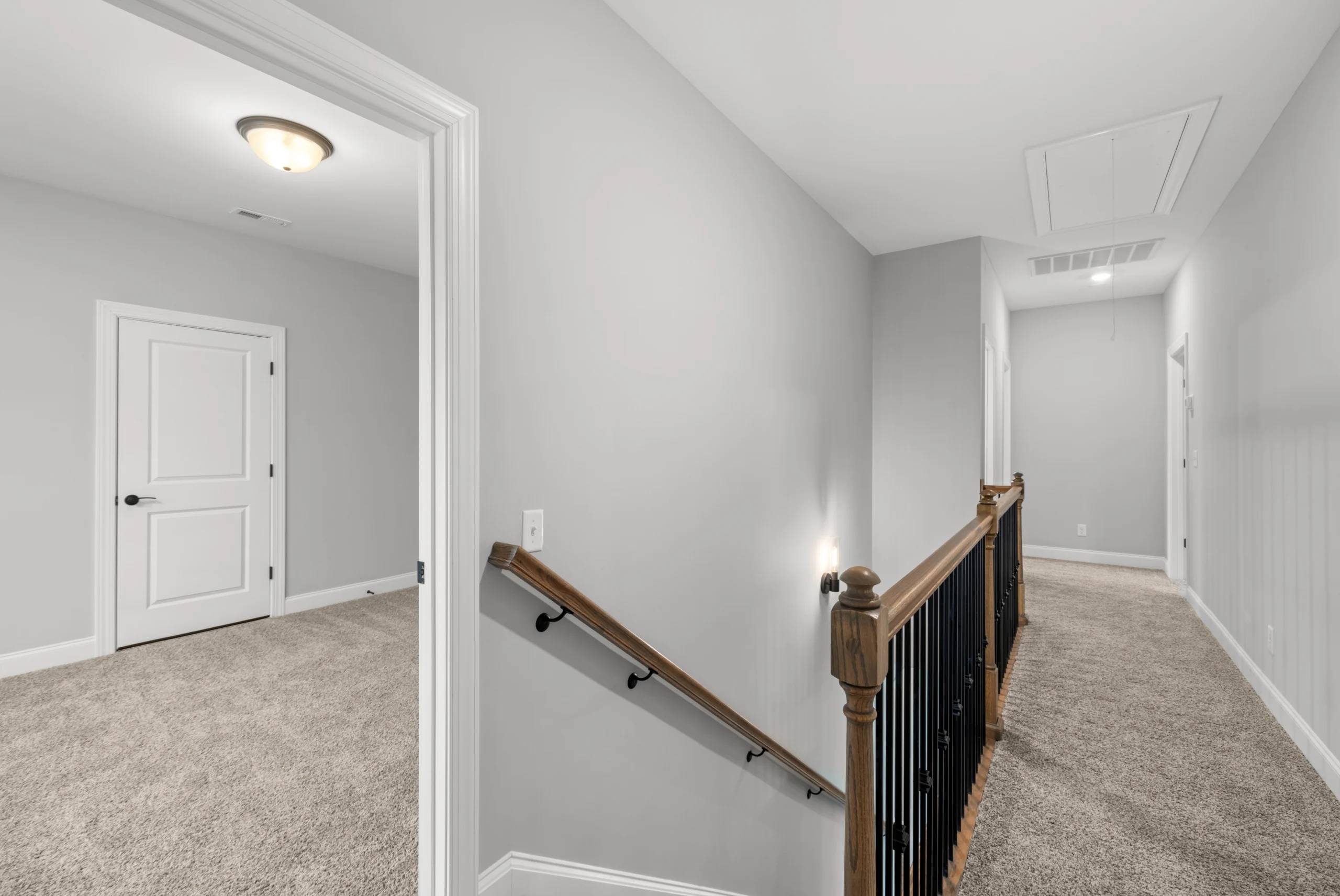 Carpeted hallway with wooden railing, leading to closed doors in a neutral-toned Pratt Home Builders residence, Chattanooga TN.