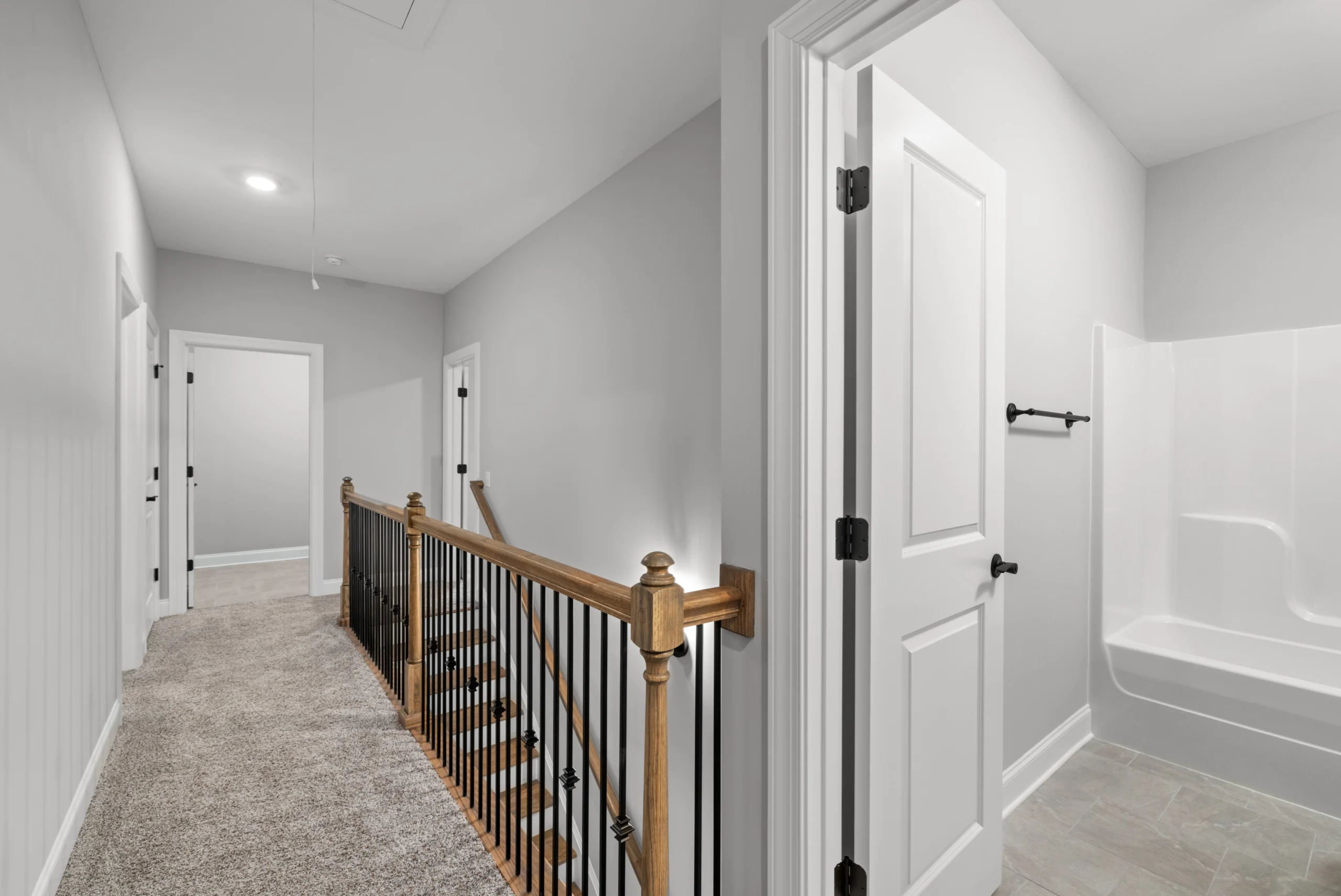 Hallway with carpeted floor, wooden railing, and a bathroom view. Design by Pratt Home Builders in Chattanooga TN.
