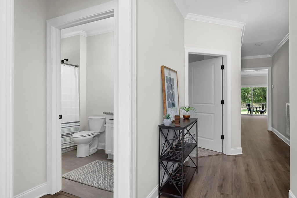 Hallway in a Pratt Home Builders property in East Brainerd, featuring a bathroom, decorative shelf, and view towards a dining area with large window