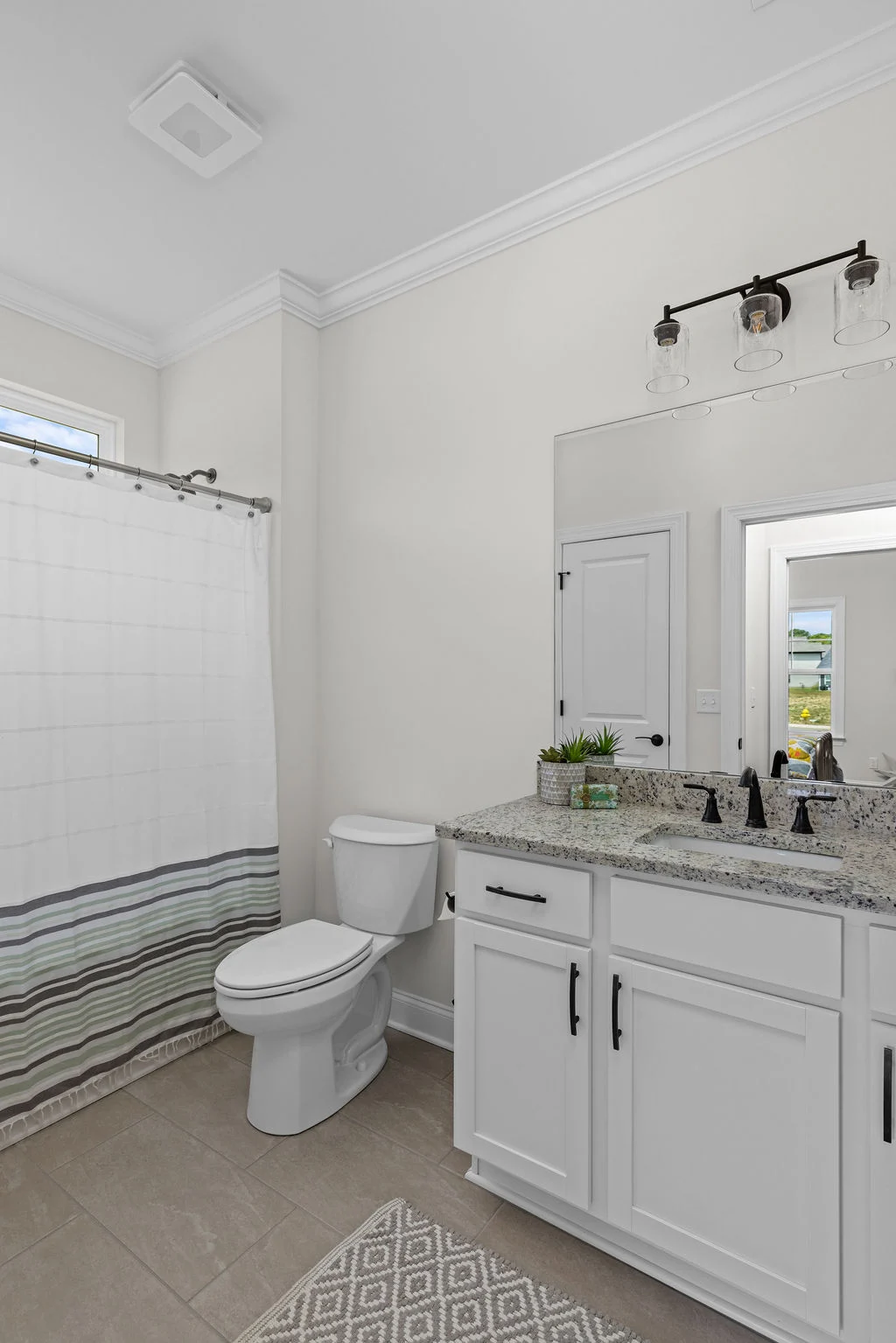 Modern bathroom with granite countertop, white cabinets, and a striped shower curtain. Designed by Pratt Home Builders in Chattanooga TN.