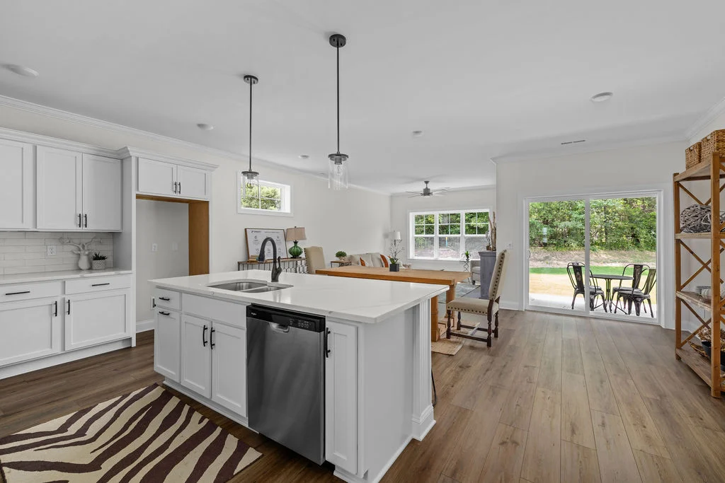 Open-concept kitchen and living area by Pratt Home Builders in Chattanooga TN. Features white cabinets, wood floors, and large windows with outdoor vi