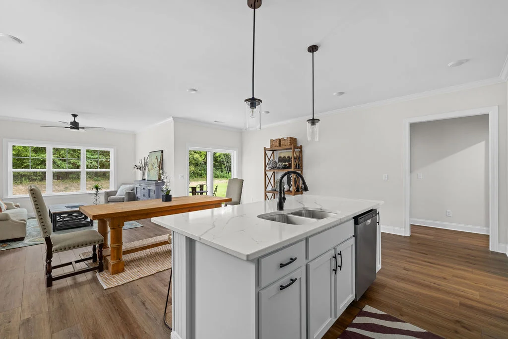 Modern kitchen with island, sink, and dishwasher; open concept to living area with large windows. Design by Pratt Home Builders in Chattanooga TN.