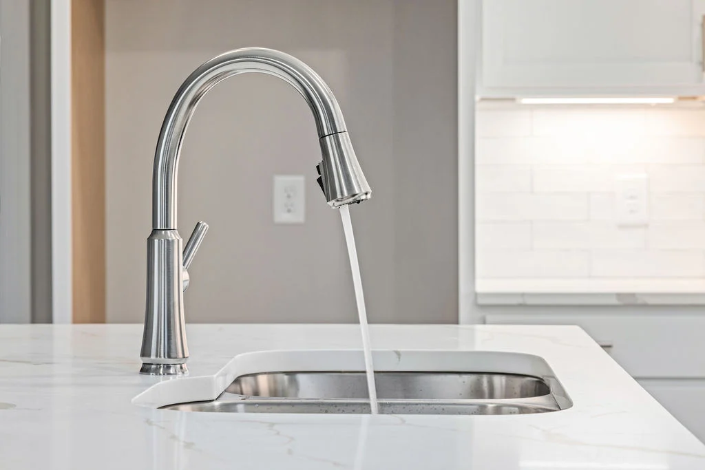 Modern kitchen faucet on granite countertop, water running into sink, featuring craftsmanship by Pratt Home Builders in Chattanooga TN.
