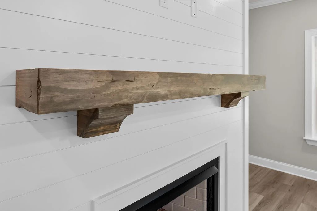 Rustic wooden mantelpiece on white shiplap wall above fireplace by Pratt Home Builders in Chattanooga TN. Minimalistic interior design.