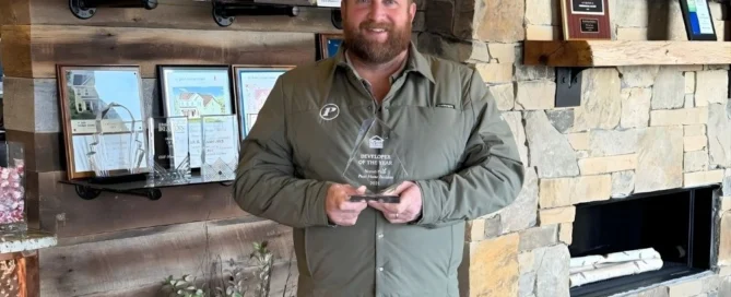 Man in green shirt holding "Developer of the Year" award from Pratt Home Builders in Chattanooga TN, standing by a stone fireplace with plaques.