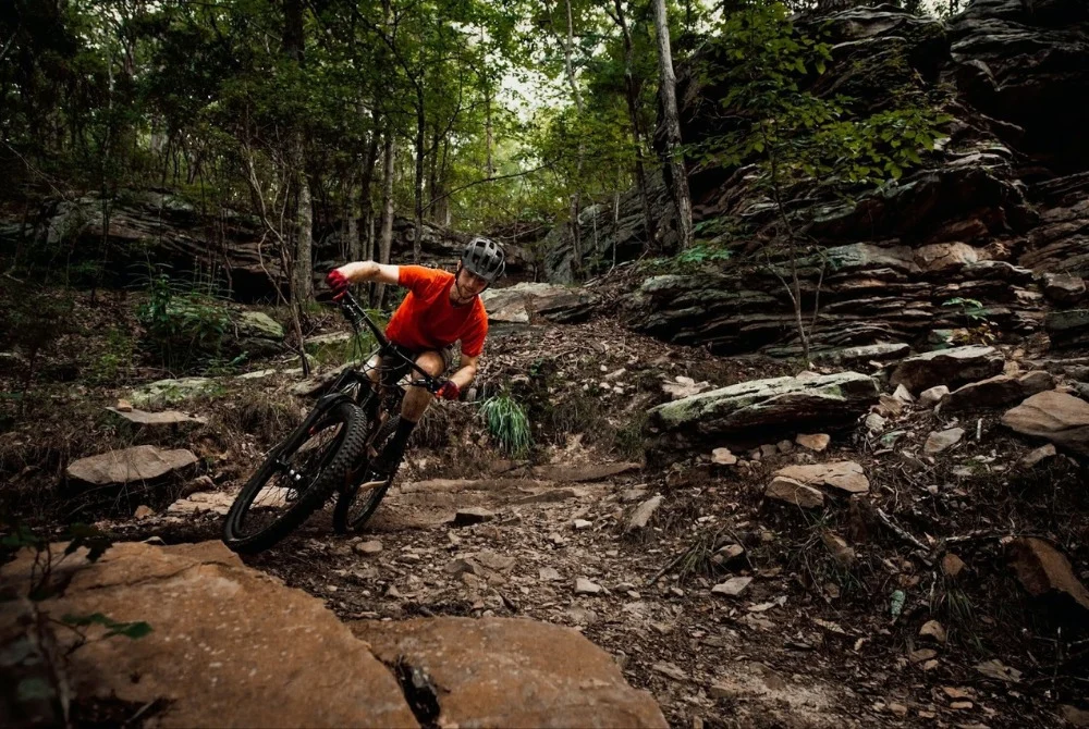 Mountain biker navigates a rocky trail in a dense forest, showcasing adventure near Pratt Home Builders in Chattanooga TN.