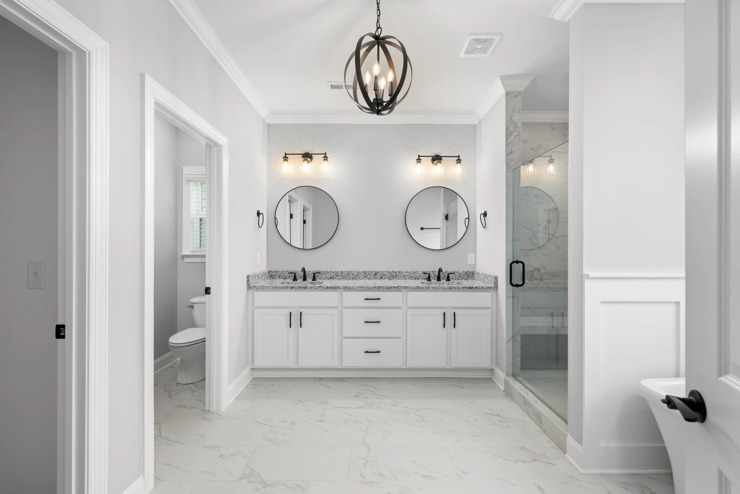New Home Chattanooga TN. Modern bathroom by Pratt Home Builders, featuring dual sinks, round mirrors, marble tiles, and a glass shower.